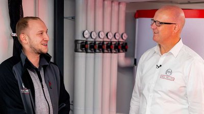 Zwei Männer stehen in einem modernen Raum, lächeln und unterhalten sich über technische Geräte und Installationen.