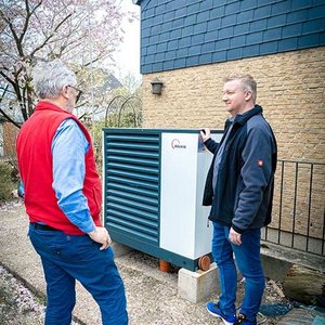 Zwei Männer stehen neben einer großen Wärmepumpe, während sie sich angeregt unterhalten und die Technik betrachten.