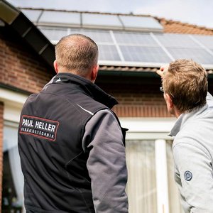 Zwei Männer betrachten die Solarpanels auf einem Dach, während sie sich angeregt unterhalten und auf die Technik zeigen.