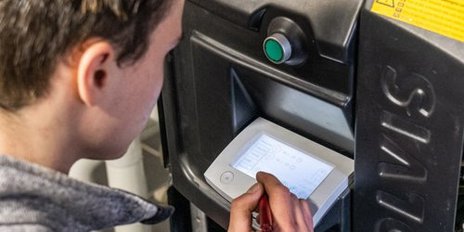 Ein junger Mann bedient ein digitales Steuergerät, während er Notizen auf einem Tablet macht, um Einstellungen zu überprüfen.