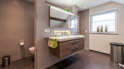 Modernes Badezimmer mit eleganter Holzschublade und Pflanzen Ein modernes Badezimmer mit einem schwebenden Waschbecken, Holzschubladen und einem großen Spiegel, der das Licht reflektiert.