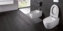 Ein modernes Badezimmer mit einem eleganten, weißen WC und einem Bidet auf einem dunklen Holzboden.