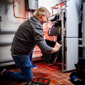 Ein Techniker kniet auf dem Boden und arbeitet an einem Heizsystem, um eine Wartung durchzuführen.