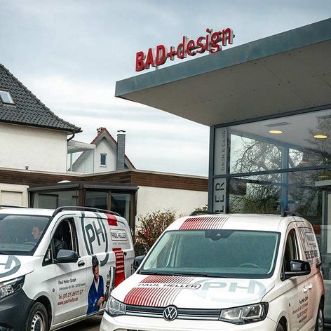 Zwei Fahrzeuge mit dem Logo von Paul Heller stehen vor einem modernen Gebäude mit einem auffälligen roten Schild.