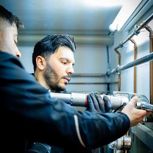 Zwei Handwerker arbeiten konzentriert an einer Rohrinstallation, während sie ein Werkzeug in der Hand halten.