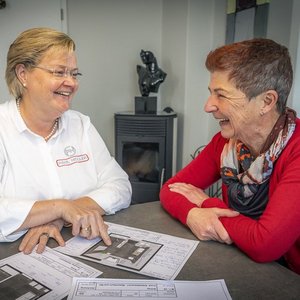 Eine Frau zeigt auf einen Plan, während die andere interessiert zuhört und beide freundlich miteinander lachen.