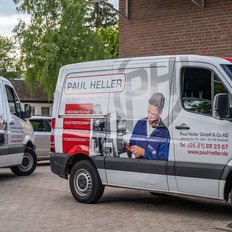 Zwei Lieferwagen der Firma Paul Heller stehen auf einem Parkplatz, umgeben von Bäumen und einem Wohngebäude im Hintergrund.