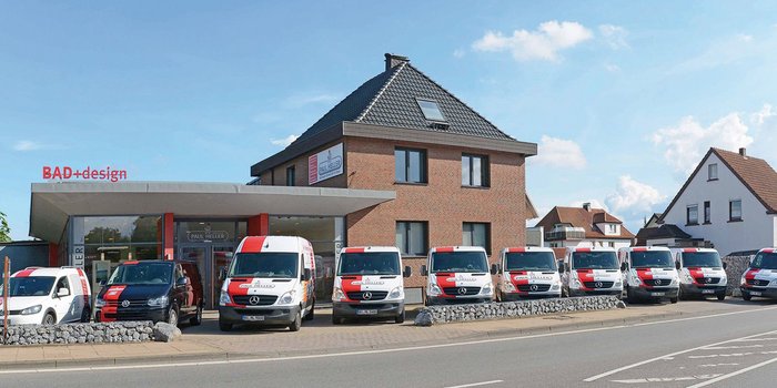 Ein modernes Geschäftshaus mit dem Schriftzug 'BAD+design' und mehreren Lieferwagen vor der Fassade auf einer sonnigen Straße.