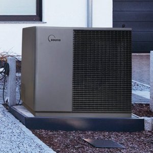 Eine moderne Wärmepumpe steht auf einem gepflasterten Bereich, umgeben von Kies und einem gepflegten Garten.